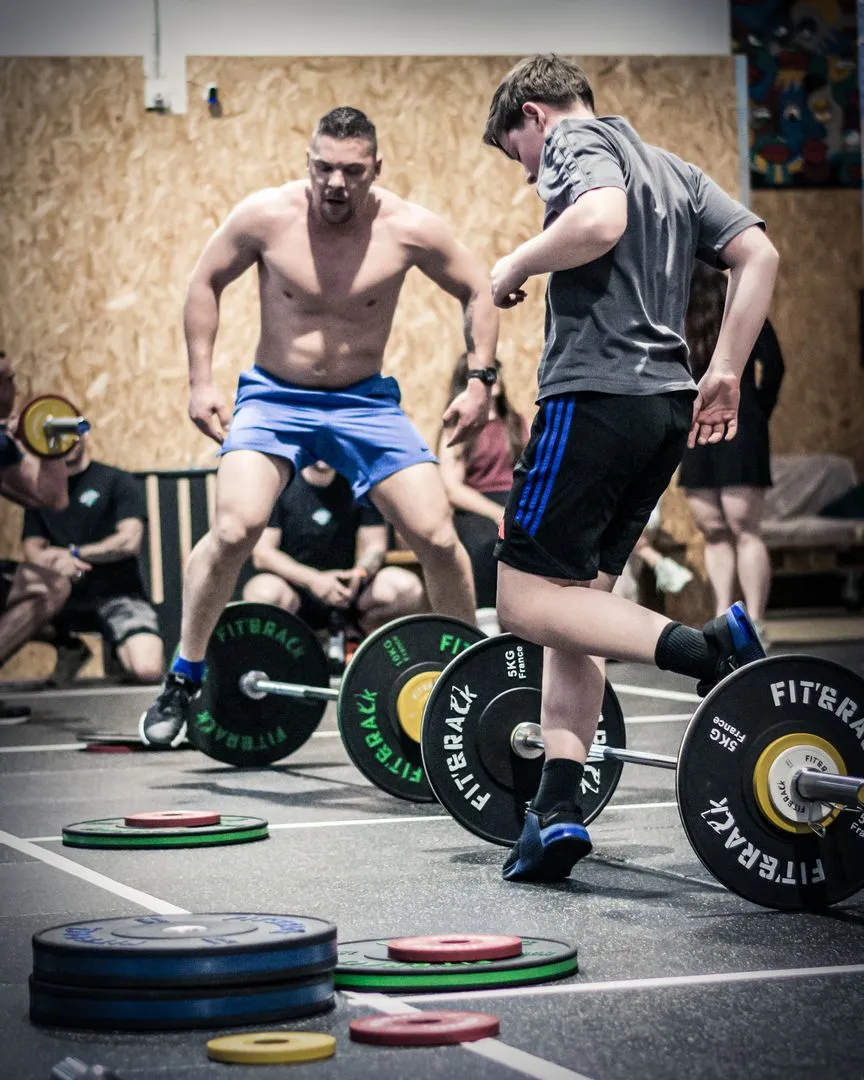 Deux hommes faisant des Lunges côte à côte en portant des haltères dans la salle de CrossFit Mazamet.